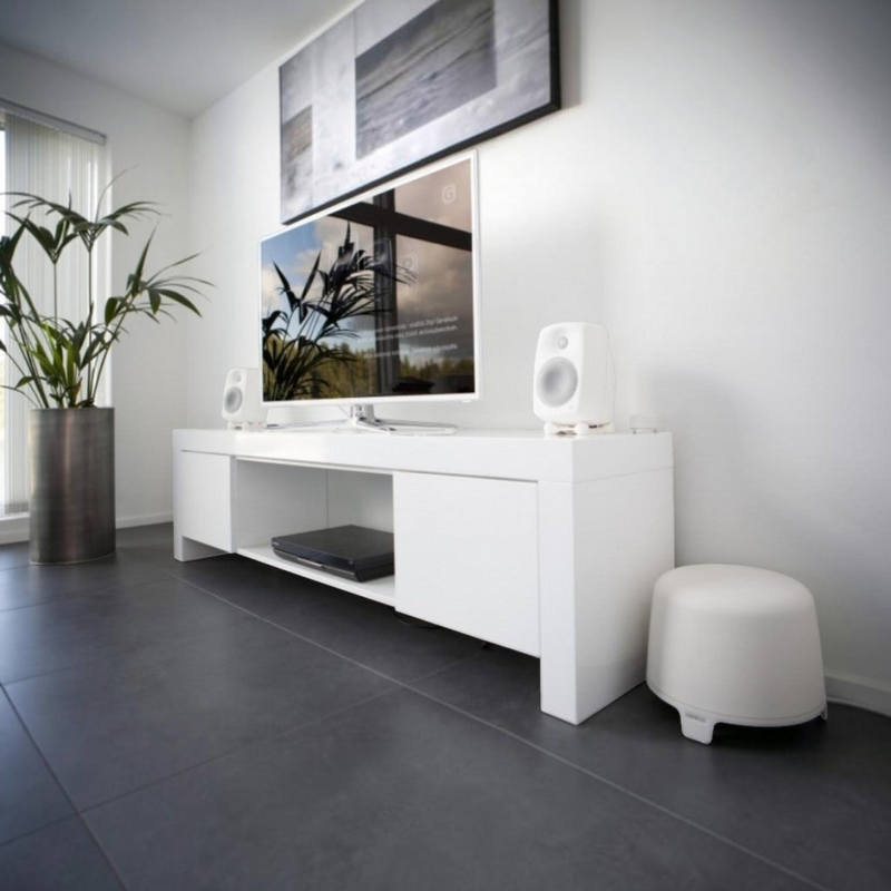 Undentia AB F One white active subwoofer placed on a dark floor in a modern living room with matching speakers
