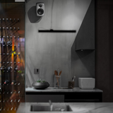 Undentia AB G Two compact active speaker mounted on a grey wall above a modern kitchen counter with a wine rack.